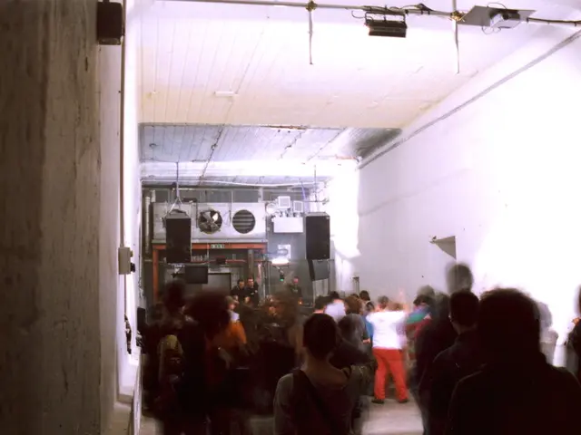 The picture is taken inside a room. In the center of the picture there are people dancing. On the...